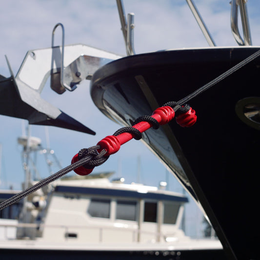 Finnish Mooring & Dock Line Shock Absorber installed on boat bow with a red snubber and black rope, with another boat in the background.